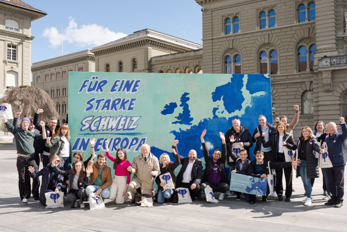 Die Europa-Allianz bestehend aus Vertreter:innen von Volt, Operation Libero, den Grünen, der Europäischen Bewegung Schweiz, VSS und weiteren vor einer Leinwand auf dem Bundesplatz. Die Leinwand zeigt eine Karte Europas, mit der fehlenden Schweiz in der Mitte. Links steht die Aufschrift: 