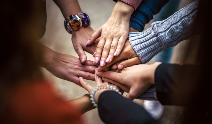 Mehrere Menschen legen ihre Hände in der Mitte aufeinander als Zeichen für Teamwork und Zusammenhalt.