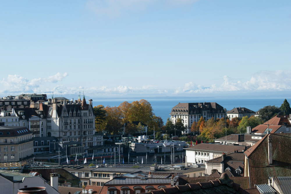 Blick von der Kathedrale in Lausanne aus über die Stadt und den See im Hintergrund. Man sieht Hausdächer von den alten Gebäuden.